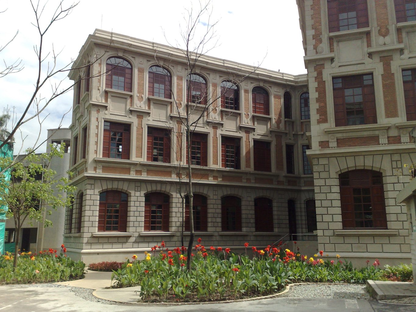 Brick and stone building with arched windows and decorative facade, beside a bed of red and yellow tulips in front.